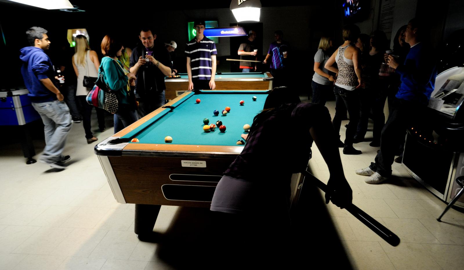 Des gens se tiennent autour d'une table de billard.