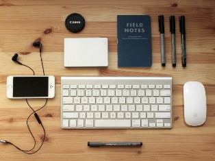 Accessoires informatiques : souris, clavier, stylos, téléphone portable, écouteurs et bloc-notes.