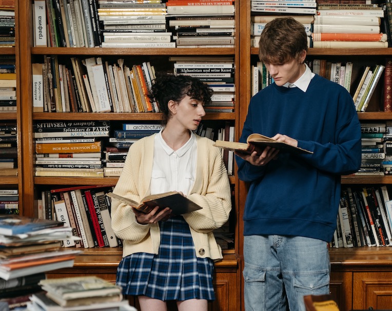 Deux étudiants debout l'un à côté de l'autre et lisant des livres dans une bibliothèque.
