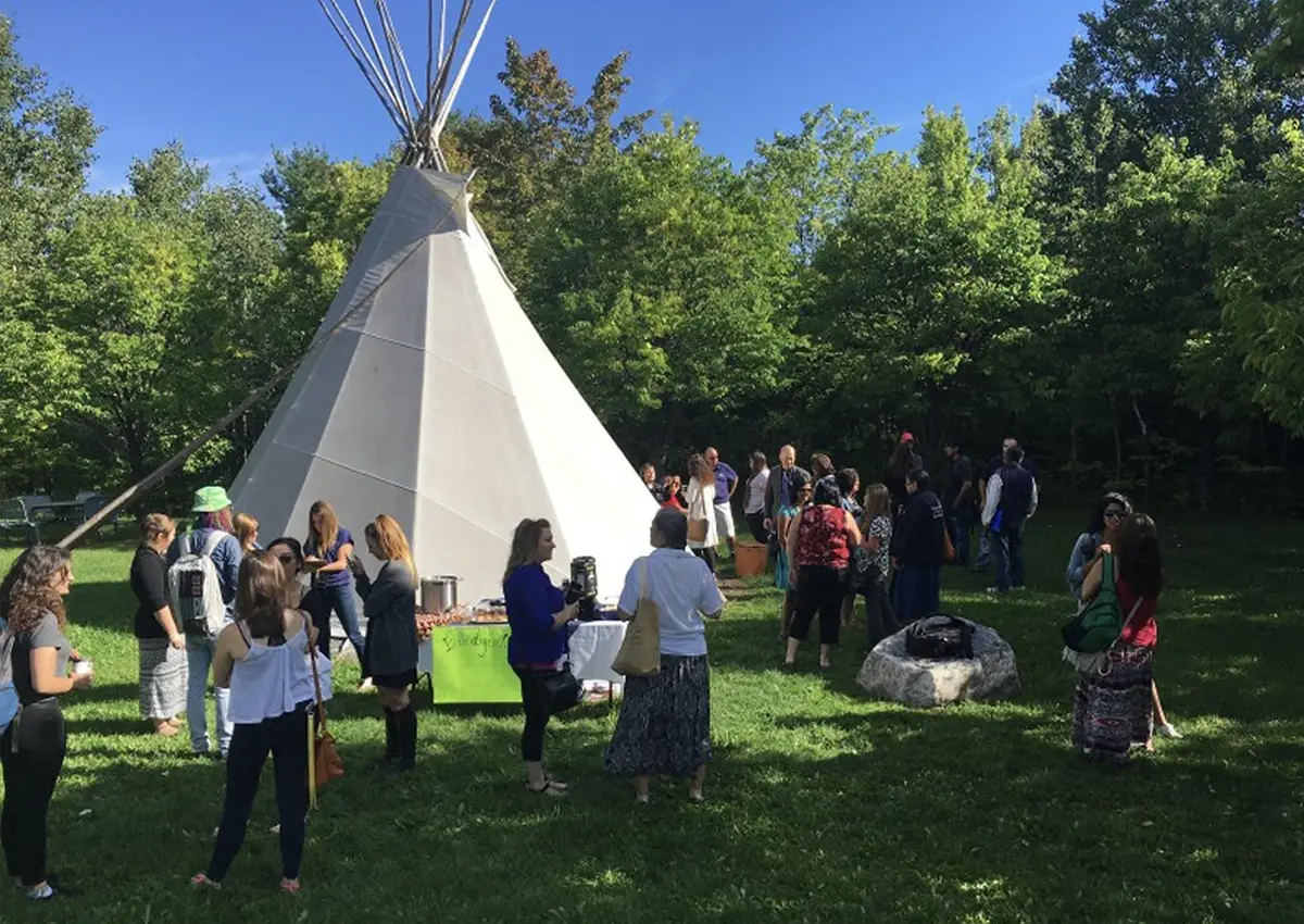 A group of people gathered on a field of grass around a tipi.