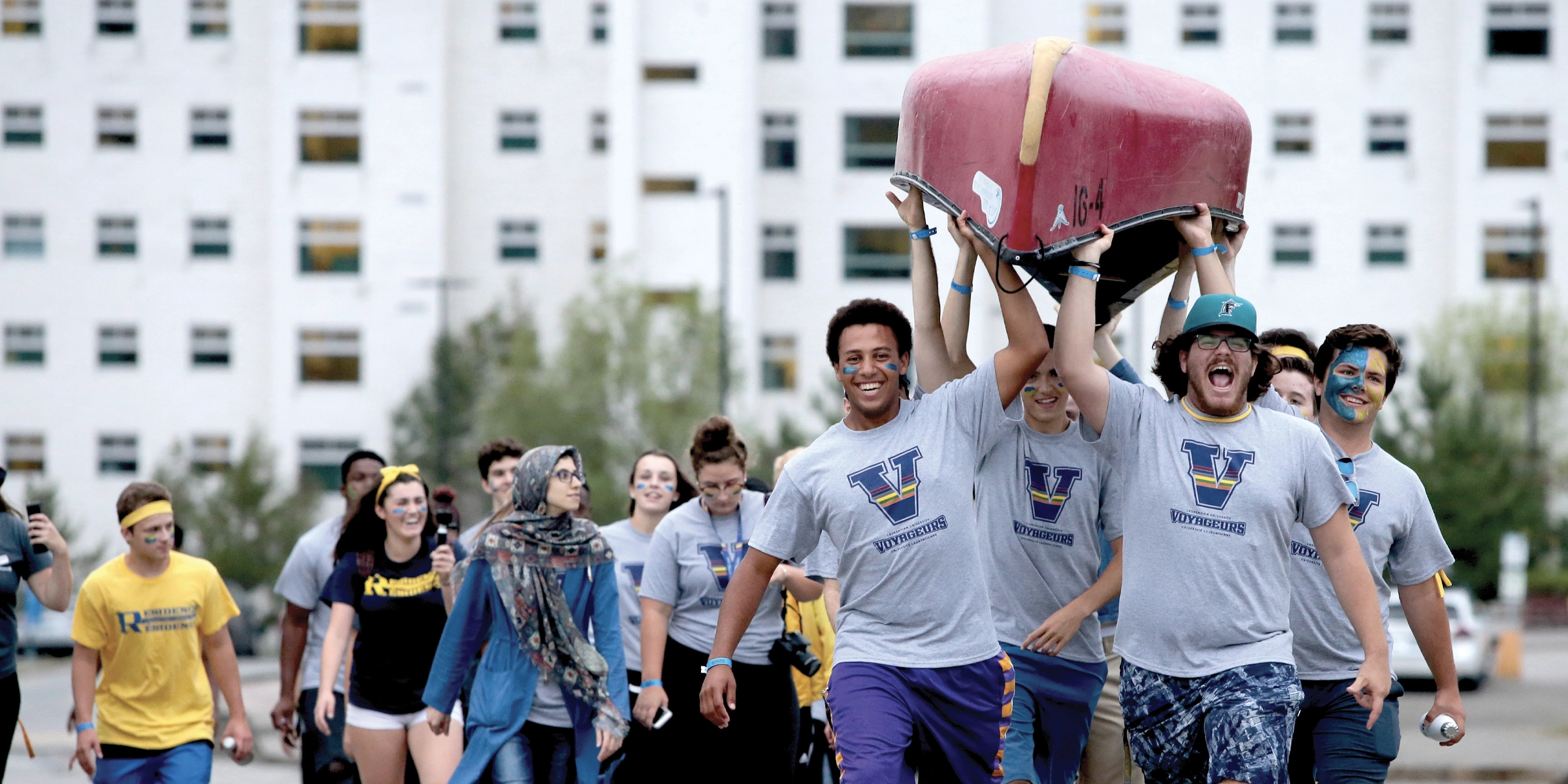 Students portaging a canoe and cheering.