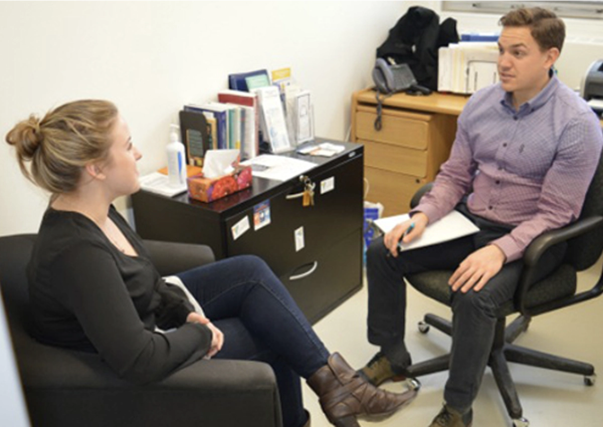 A woman sitting across from a man, speaking to one another.