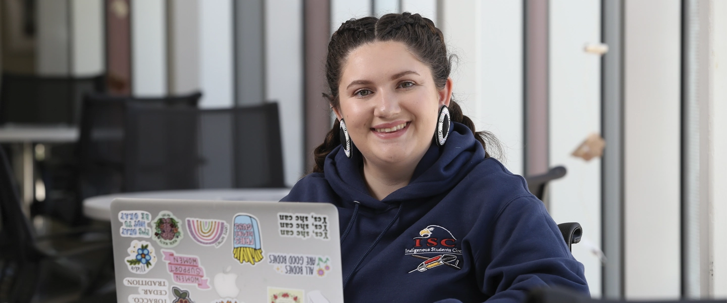 A Laurentian University student using a laptop, smiling at the camera.