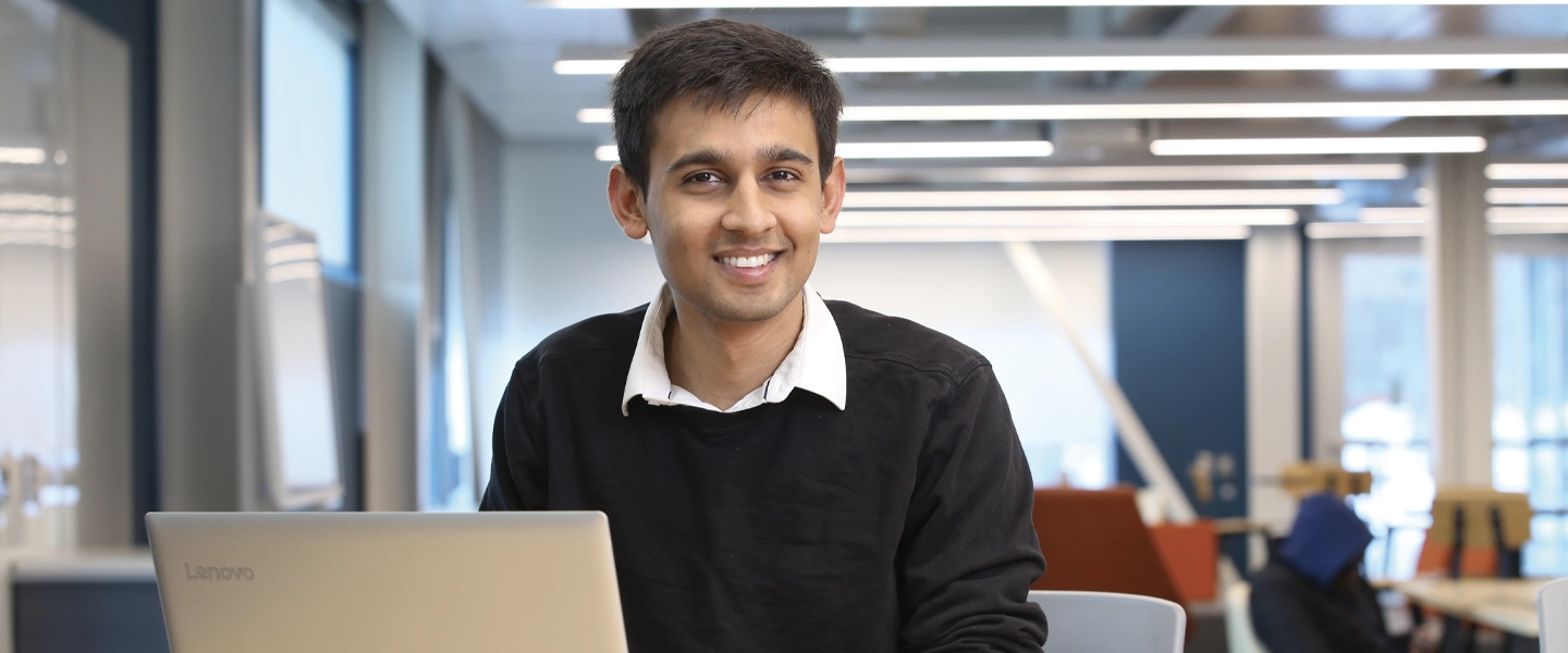 Un étudiant de l'Université Laurentienne utilisant un ordinateur portable, souriant à la caméra.