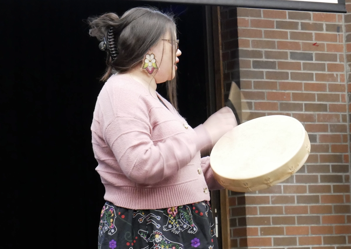 A young woman playing a drum at an Indigenous event.