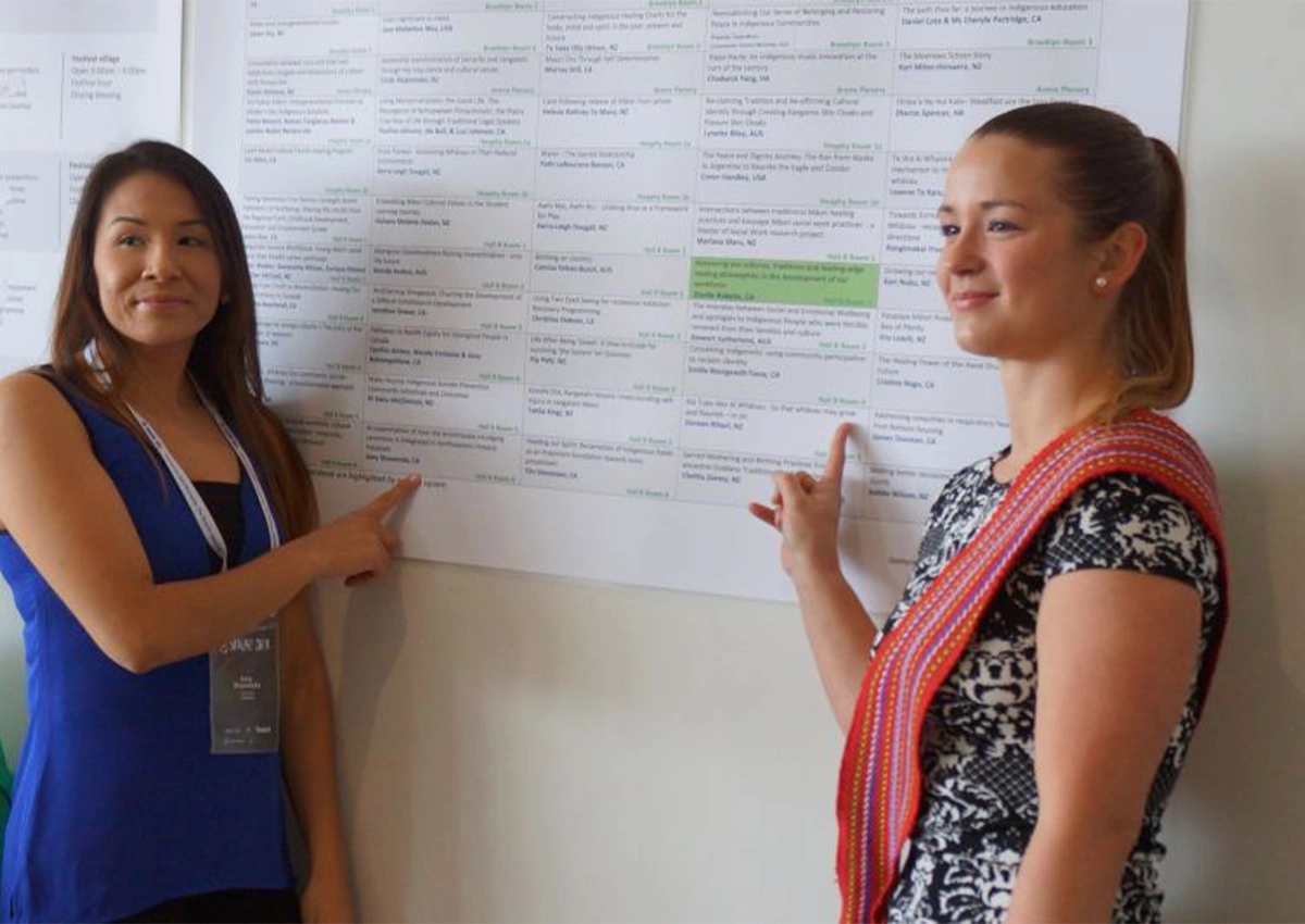 two masters students point at a poster on the wall
