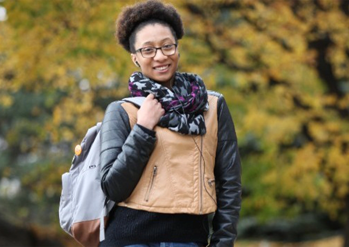 Un étudiant marche dehors par une journée ensoleillée d'automne, tout sourire.