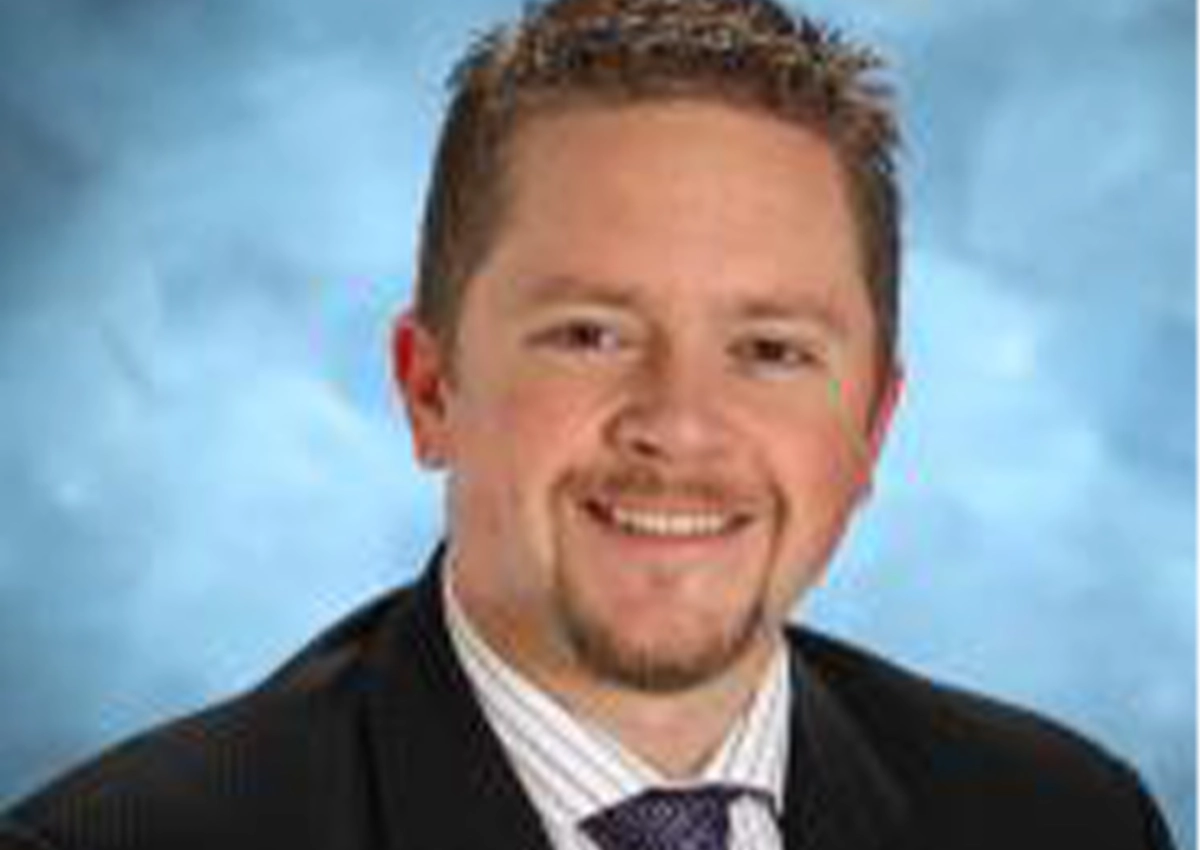 Anthony Church's headshot. he is smiling at the camera with a blue backdrop behind him. 