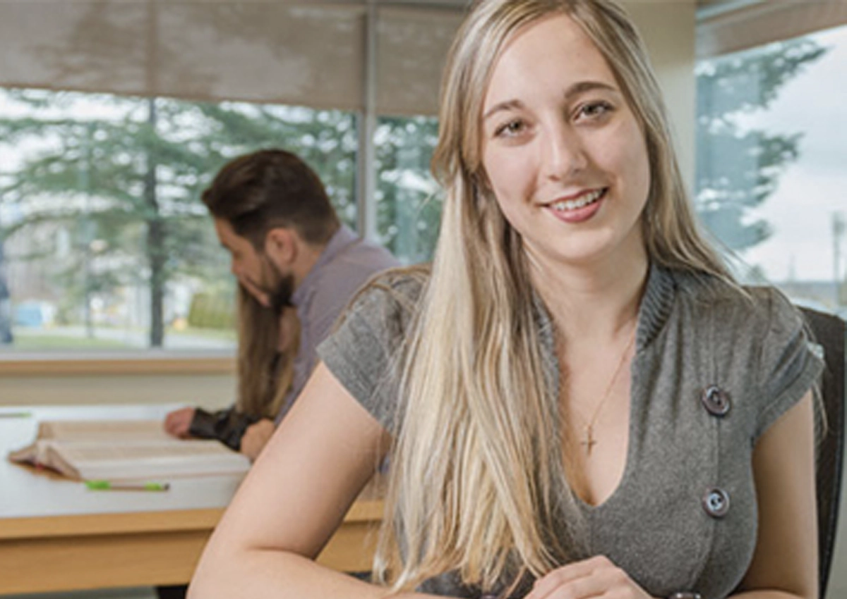 Jeune femme assise à un bureau, souriant à la caméra.