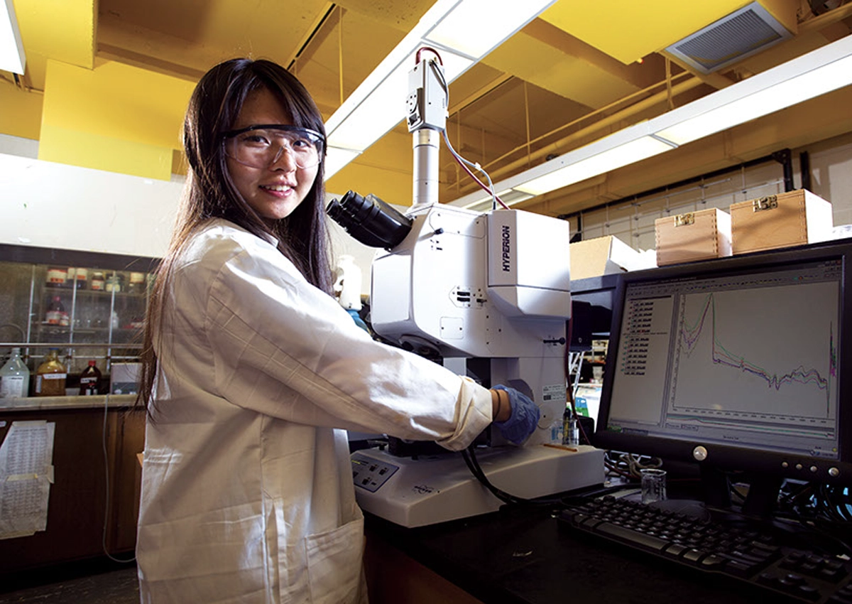 Jeune femme portant une blouse de laboratoire, travaillant avec un microscope.