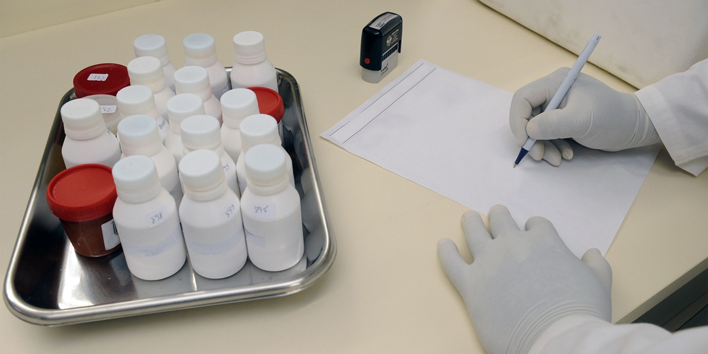 Un technicien de laboratoire écrivant sur une feuille de papier, avec un plateau de flacons à côté de lui.