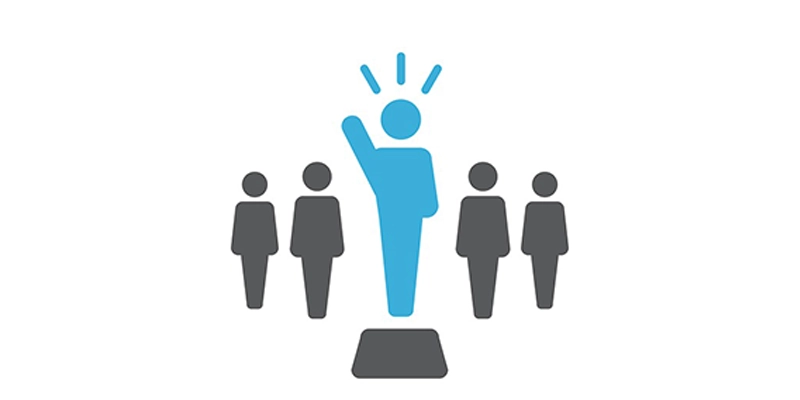 Une personne debout sur un podium, la main levée, avec d'autres personnes debout derrière elle en silence.