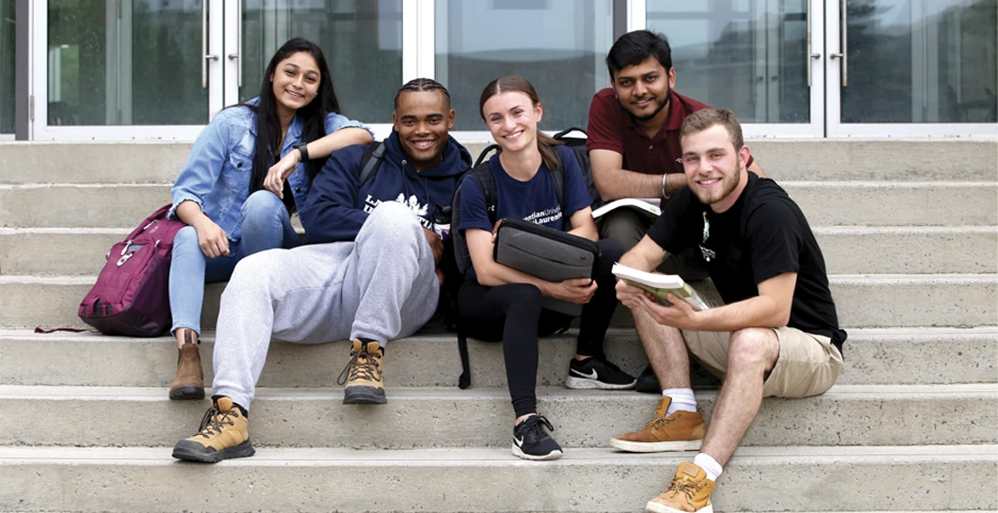 Laurentian students sitting on the steps of the Parker Building, smiling.