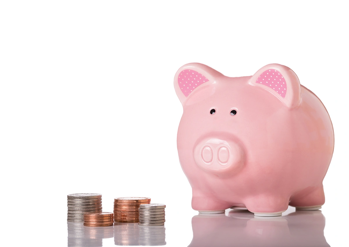 A pink piggy bank with some coins next to it.
