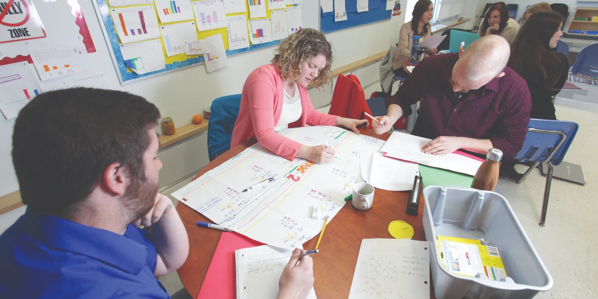 Un enseignant supervise deux élèves qui travaillent sur un devoir à une table.  