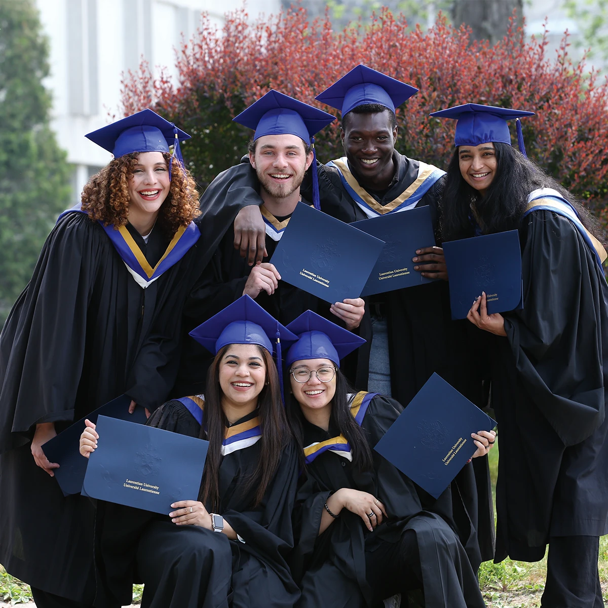 Laurentian University graduates in their graduation robes and smiling.