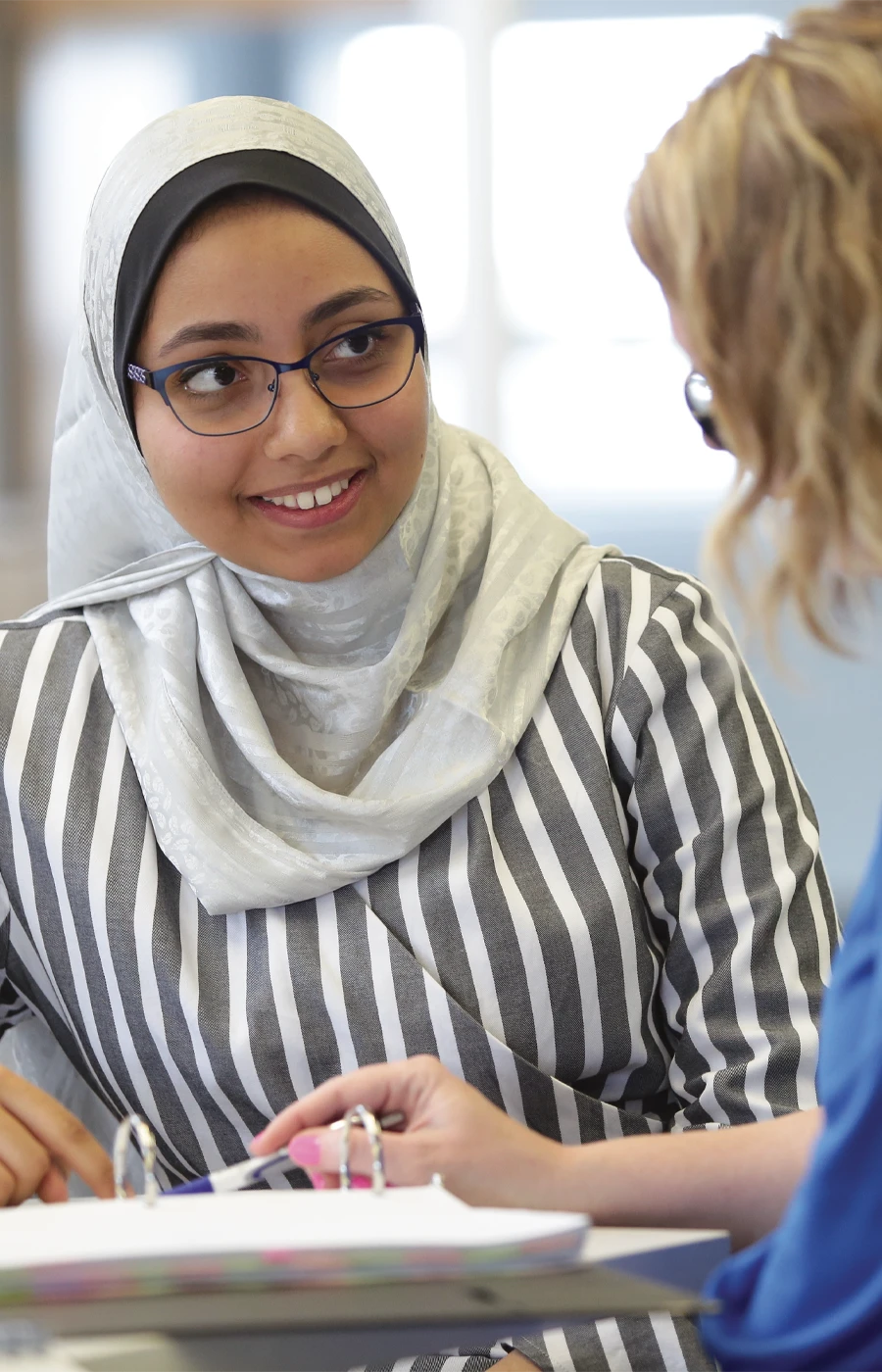 A young woman wearing a hijab smiles at a Laurentian University employee.
