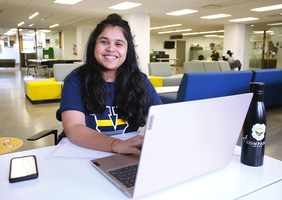 A Laurentian University student on her laptop and smiling on the second flood of the R.D. Parker Building.