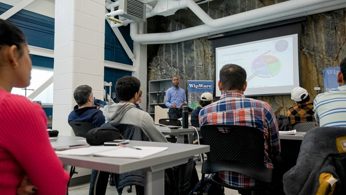 Group of students listening to a presentation, a rock wall is in the background in this lab
