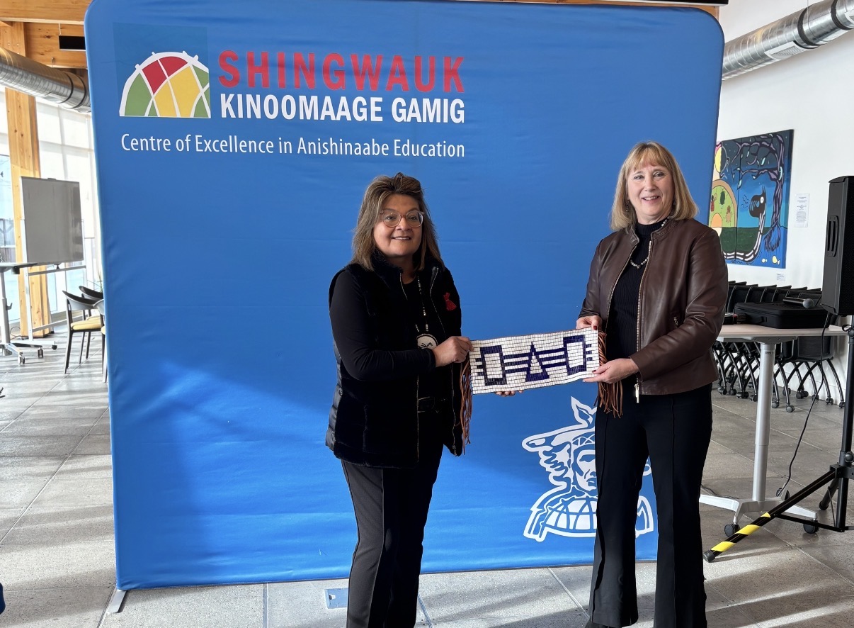 Mary Wabano-McKay, President and CAO of Shingwauk Kinoomaage Gamig, and Lynn Wells, President of Laurentian University, holding a purple and white Wampum belt. 