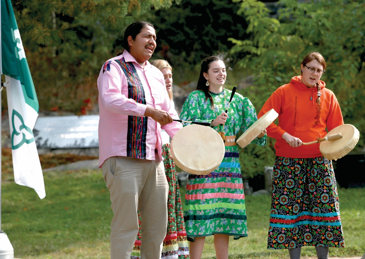 Indigenous people drumming with a Franco-Ontarian flag in the background.