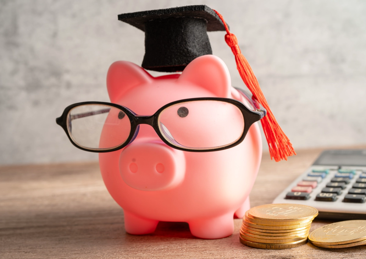 A piggy bank wearing glasses and a graduation cap.