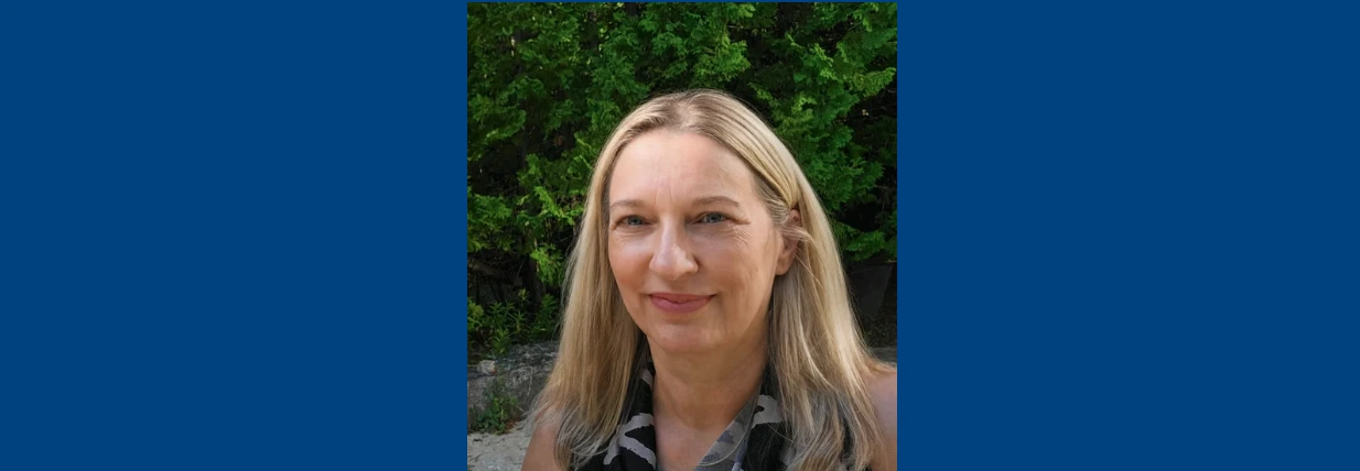 Close-up headshot of Dr. Marion Maar outdoors, smiling with lush green foliage in the background. 