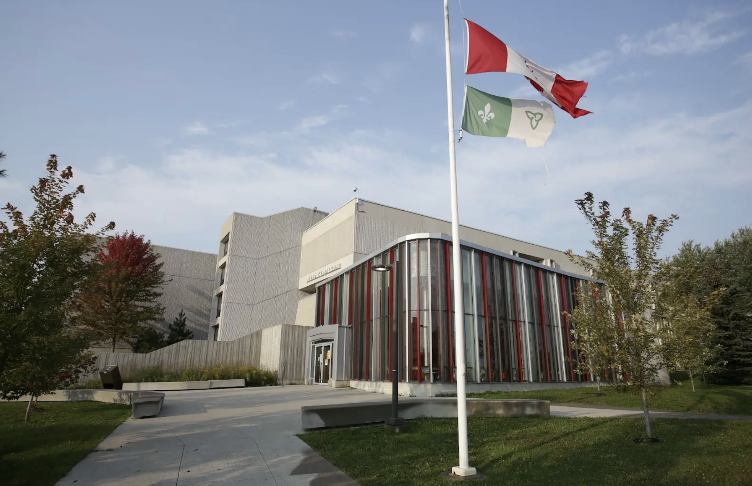 The exterior of Laurentian university on a sunny day, with the Canadian and Franco-Ontarian flags flying in the foreground.