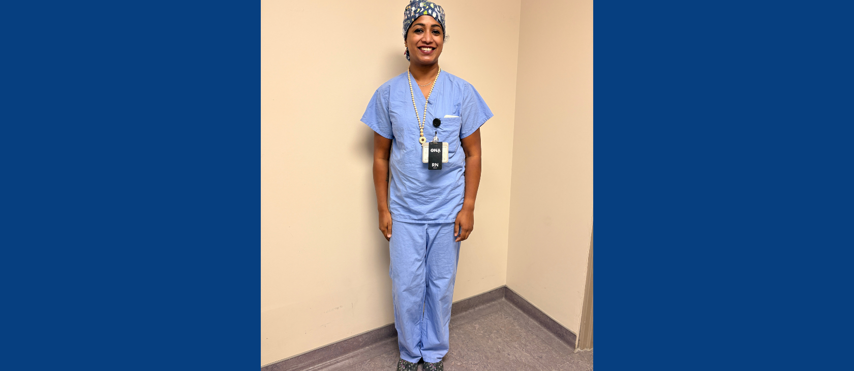Shincy Shaji standing in light blue medical scrubs, surgical cap, and RN badge.