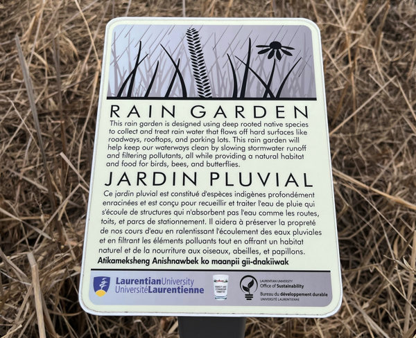 La plaque du Jardin Pluvial, qui lit « Ce jardin pluvial est constitué d'espèces indigènes profondément enracinées et est conçu pour recueillir et traiter l'eau de pluie qui s'écoule de structures qui n'absorbent pas l'eau comme les routes, toits, et parcs de stationnement. Il aidera à préserver la propreté de nos cours d'eau en ralentissant l'écoulement des eaux pluviales et en filtrant les éléments polluants tout en offrant un habitat naturel et de la nourriture aux oiseaux, abeilles, et papillons.