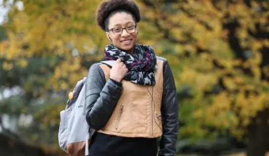 Student with glasses holding backpack and smiling at camera