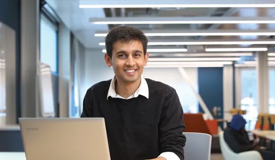 Un étudiant assis à son pupitre avec un ordinateur portable, souriant.