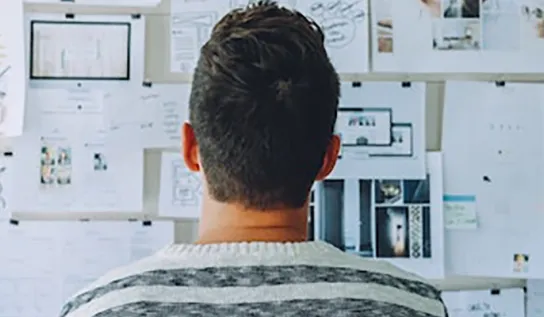 a man looking at a wall covered in papers with his back to the camera