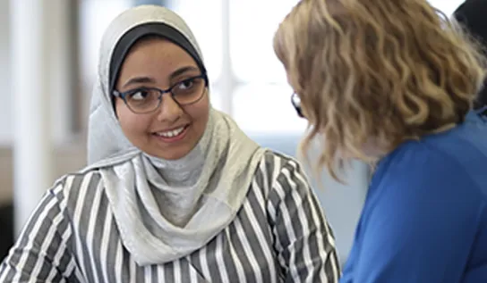 A young woman wearing a hijab, smiling at a university employee.