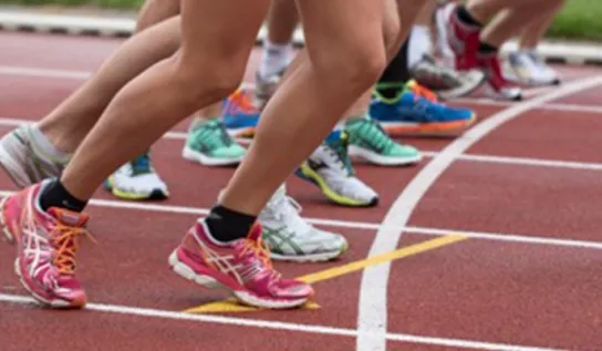 Des personnes dont on ne voit que les jambes sont alignées au départ d'une piste de course.