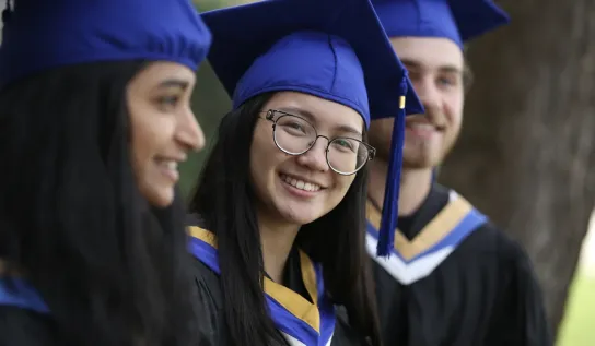 Trois étudiants vêtus d'une tenue de cérémonie noire, bleue et jaune, souriants.