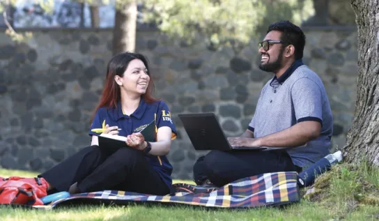Deux étudiants de l'Université Laurentienne étudient sur l'herbe à l'extérieur.