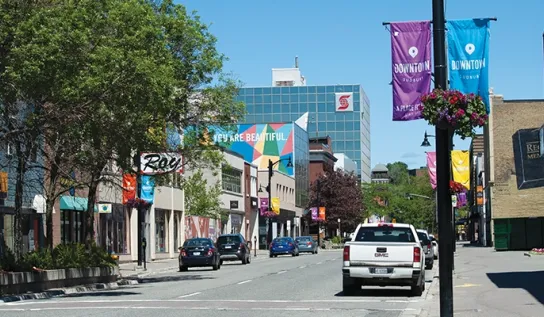 Une rue du centre-ville de Sudbury, avec des voitures garées sur le côté et un bâtiment orné d'une fresque murale « You are beautiful » (Tu es belle).