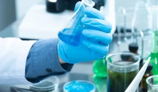 A lab technician in a lab holding a beaker of blue liquid.