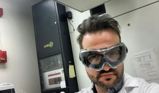 Erik Emilson wearing safety goggles and a white lab coat giving a thumbs up