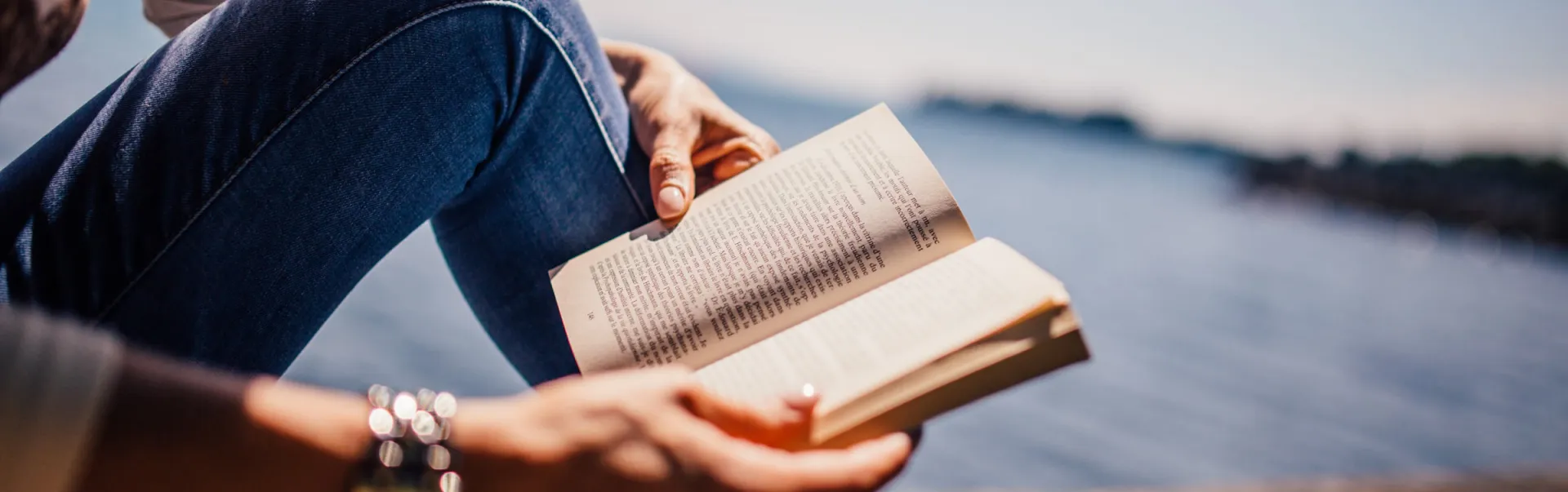 Student reading a book by the water