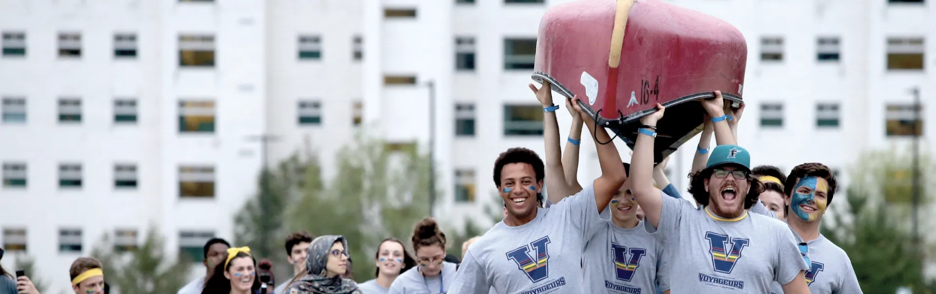 Students portaging a canoe and cheering.