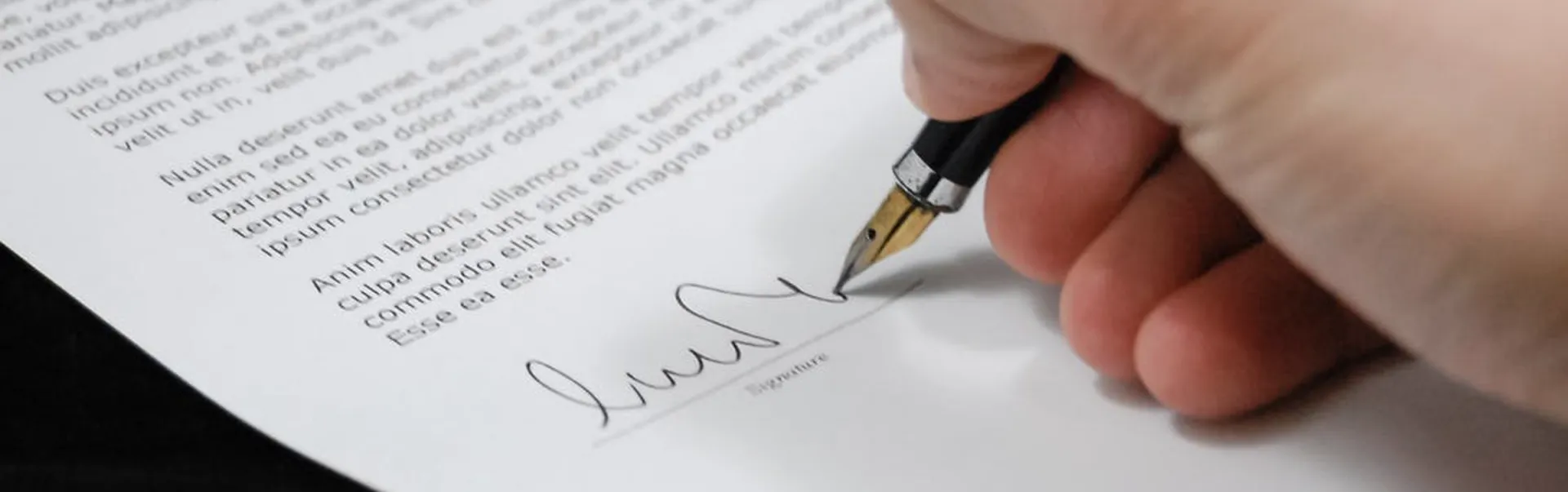 A hand holding a pen, signing a piece of paper.