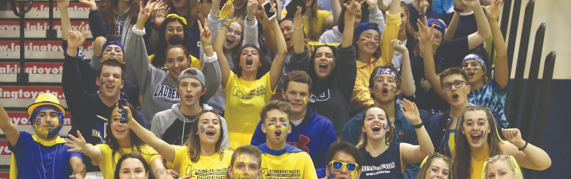 A group of Laurentian students proudly cheer in the Ben Avery Gym. They are wearing yellow and blue to proudly cheer on their team. 