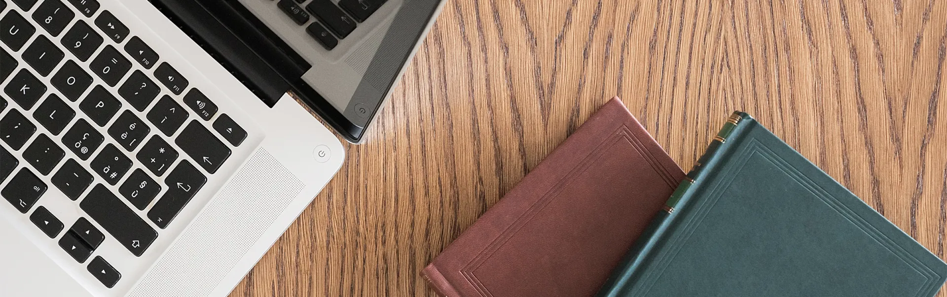 A laptop open on a desk, with green and brown notebooks placed next to it.