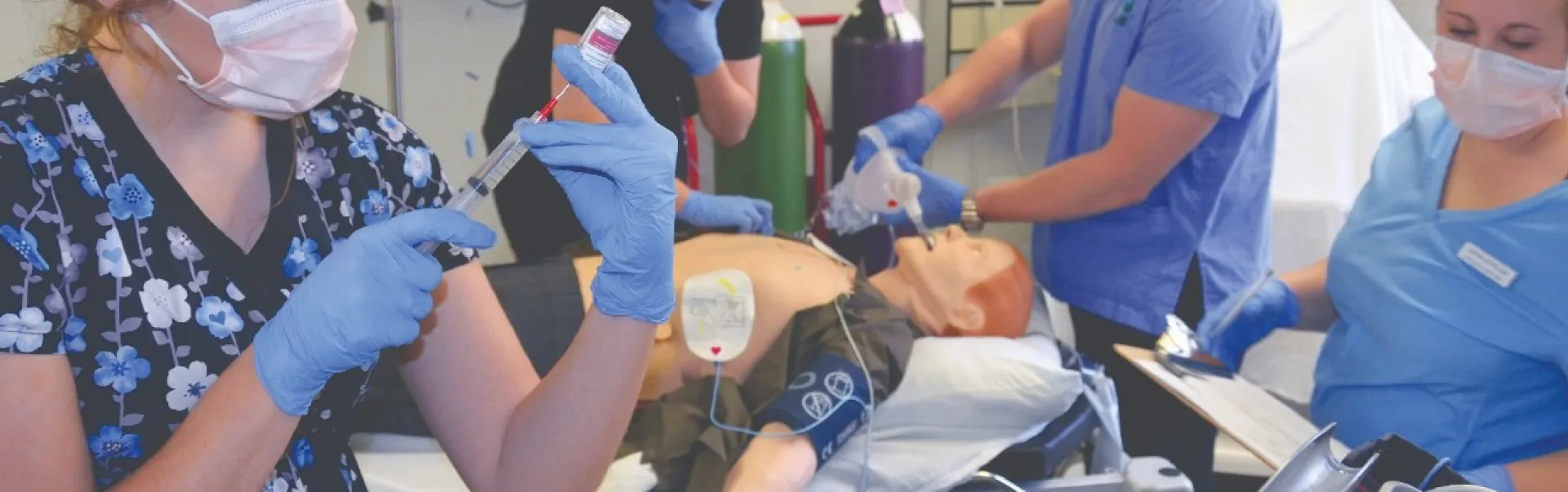 Nursing students are smiling while around a patient that is lying on a bed