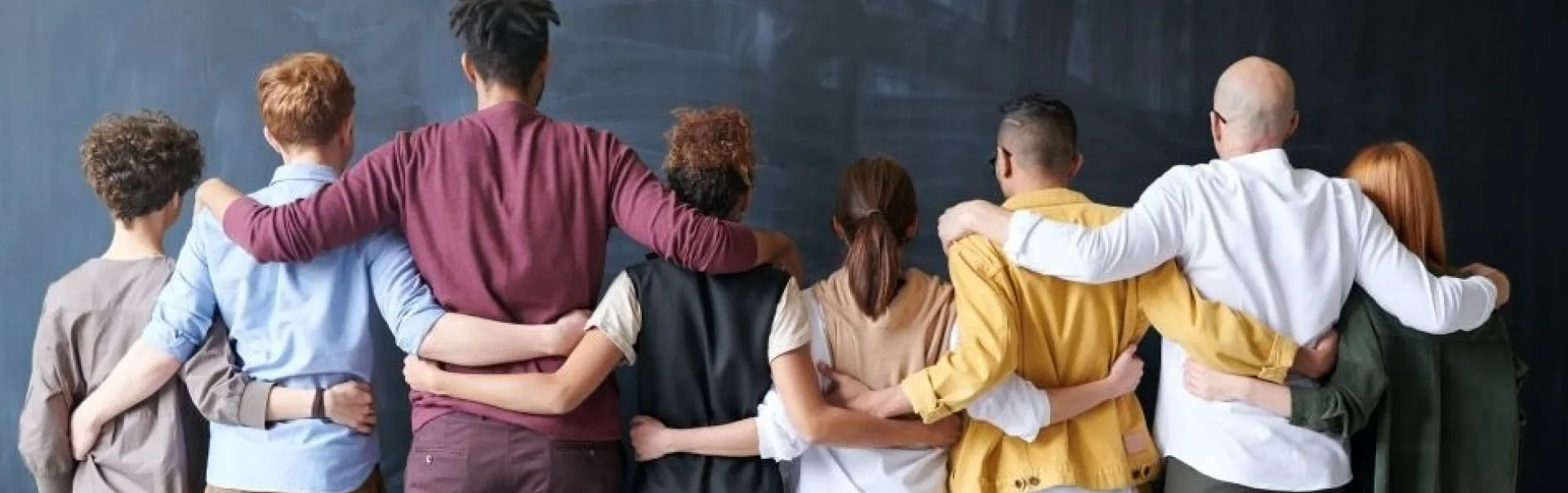A group of people placing each others arms on their shoulders, making a line