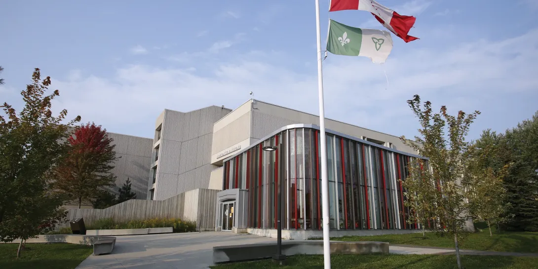 Édifice Alphonse-Raymond avec les drapeaux canadien et franco-ontarien flottant sur le mât à l'extérieur.
