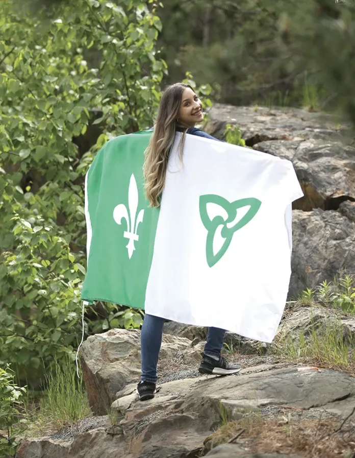 A girl standing on a large rock, holding the Franco-Ontarian flag.