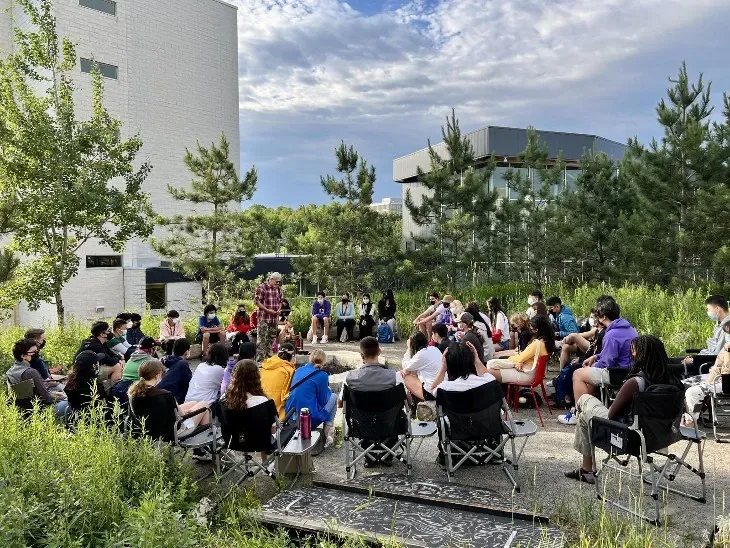 Un groupe de personnes assises sur des chaises de jardin près d'un foyer extérieur.